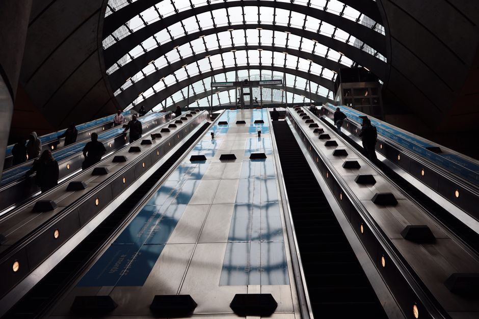 The image depicts a modern indoor space with a large, oval-shaped glass ceiling composed of multiple curved glass panels supported by teal-colored metal framework, allowing natural daylight to illumin